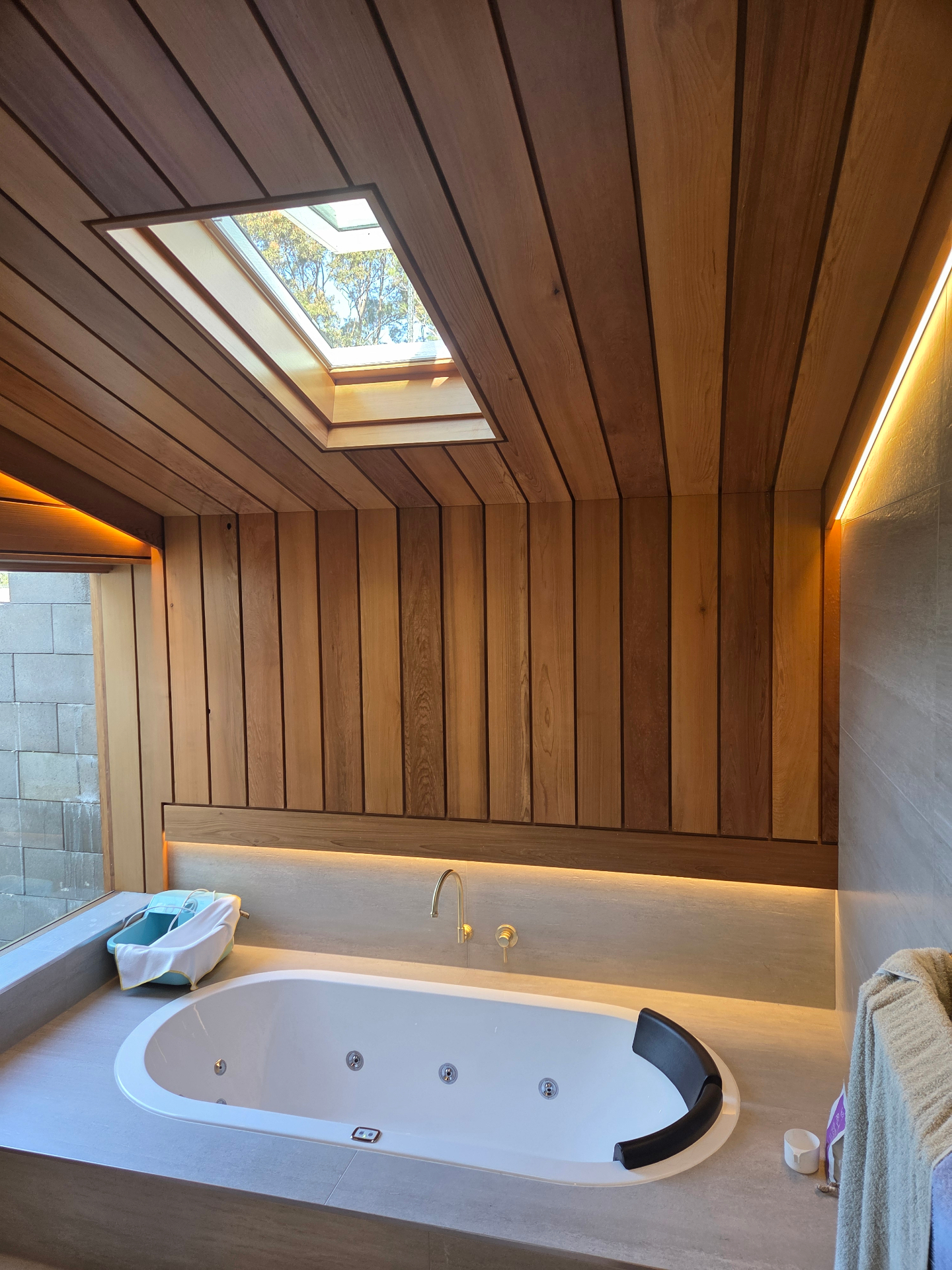Timber-lined bathroom with skylight, stone benchtop and concealed LED lighting
